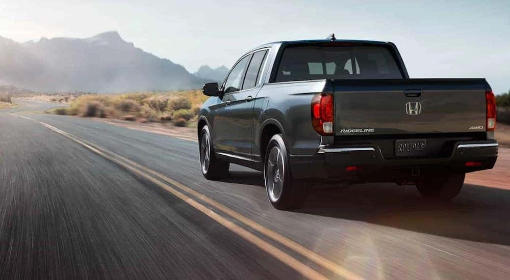 Back view of a grey 2020 Honda Ridgeline driving down a mountain-lined road