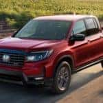 A red 2021 Honda Ridgeline is shown from the front at an angle while driving down a dirt road after the owner searched 'used trucks for sale'.