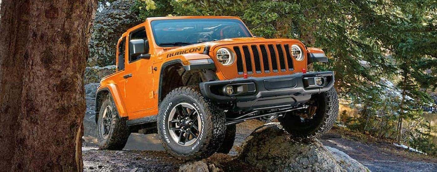 Front view of an orange 2019 Jeep Wrangler driving over a large rock
