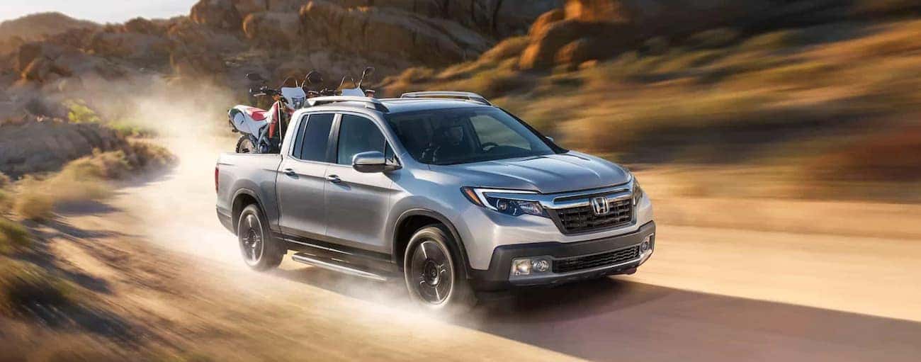 A silver 2020 used Honda Ridgeline for sale is shown speeding on a dusty dirt road.