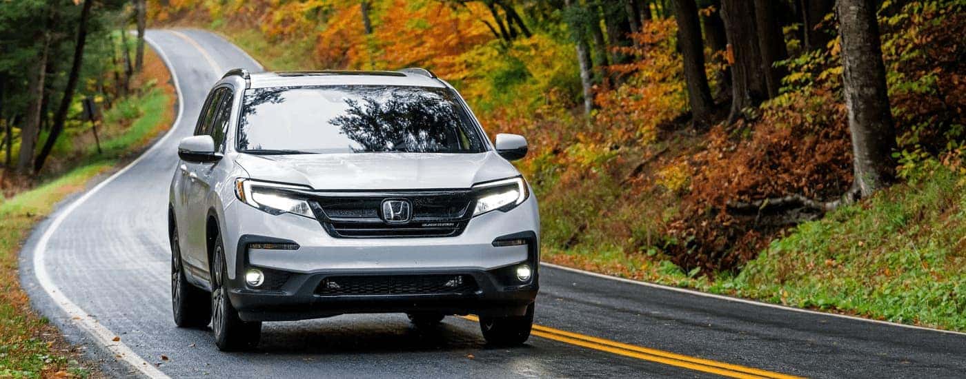 A white 2022 Honda Pilot Black Edition is shown driving on an open road during the fall season.