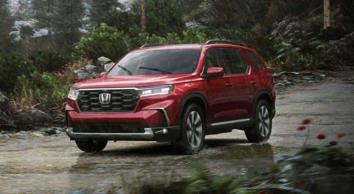 A red 2023 Honda Pilot Elite is shown driving in the rain.