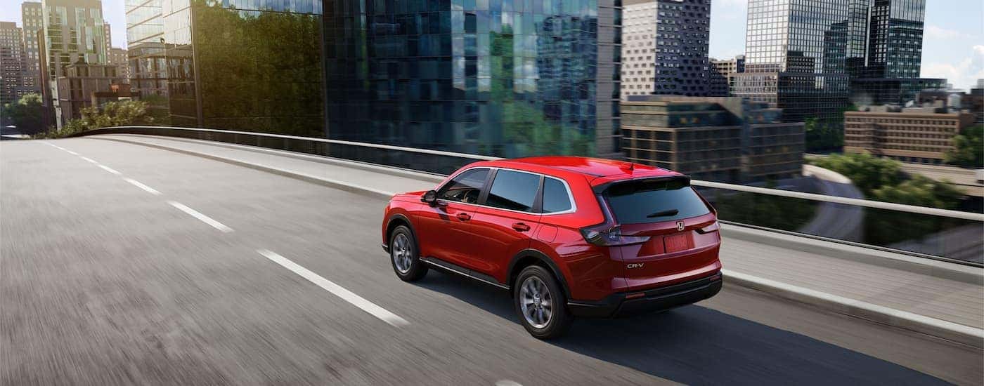 A red 2023 Honda CR-V EX is shown from a rear angle driving on a city highway.