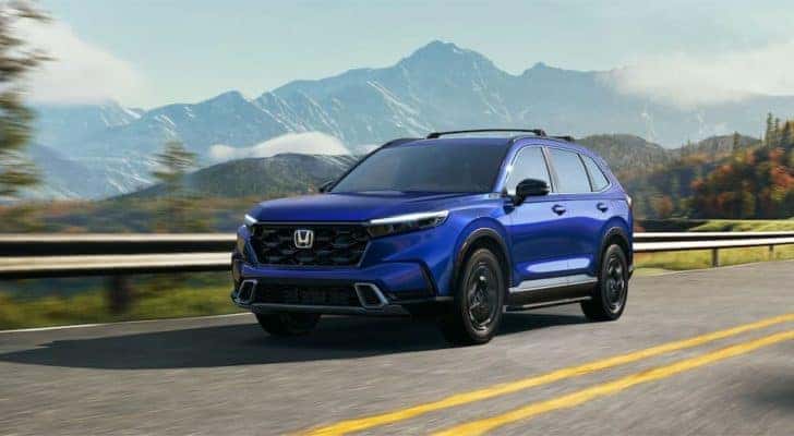 A blue 2023 Honda CR-V Sport Touring is shown driving on a highway with a mountain view.