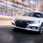 A white 2020 Honda Accord is shown driving through a city street at dusk