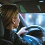 A blonde woman holds a steering wheel while driving a car