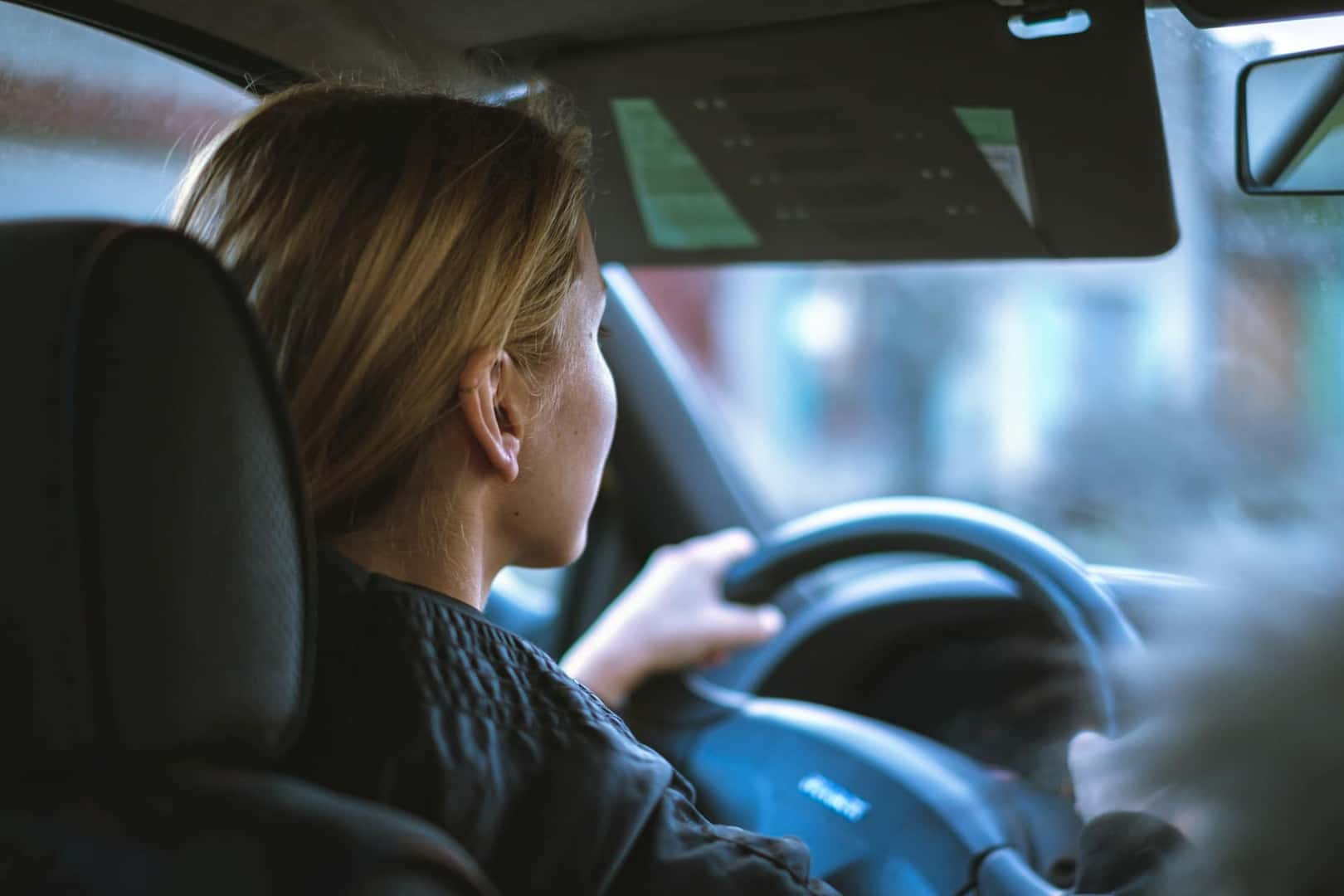 A blonde woman holds a steering wheel while driving a car
