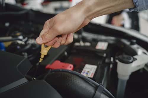 Hand checking oil dipstick in a car engine bay for maintenance and diagnostics