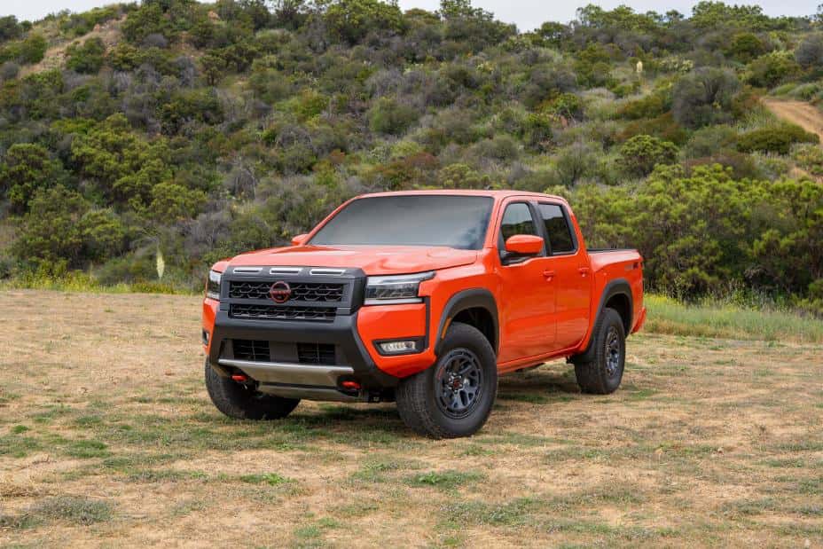 orange nissan frontier parked on dry grass in nature frontview