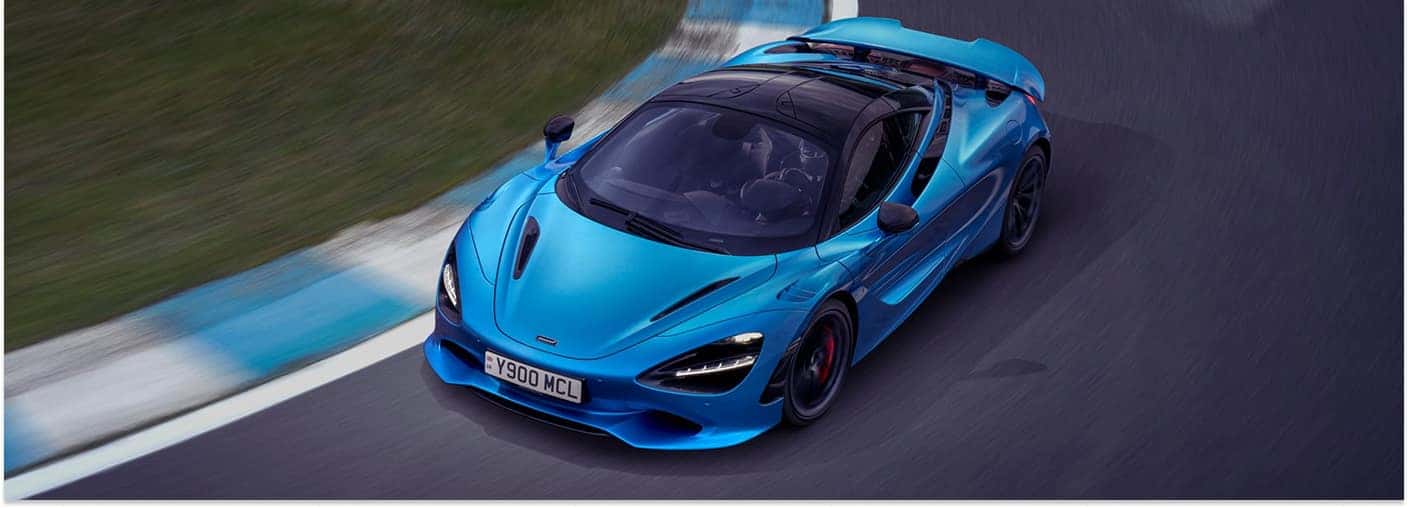 Option 1: Overhead front three-quarter view of a blue 2026 McLaren 750S driving on a racetrack.