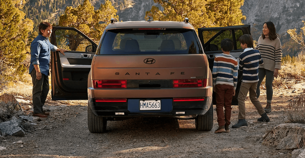 Family standing by the rear of a 2026 Hyundai Santa Fe Hybrid, parked in the mountains