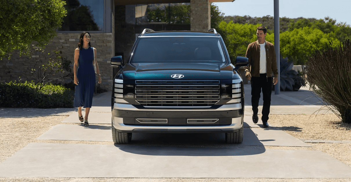 Front view of the 2026 Hyundai Palisade with a man and woman walking toward the SUV in a modern driveway setting.