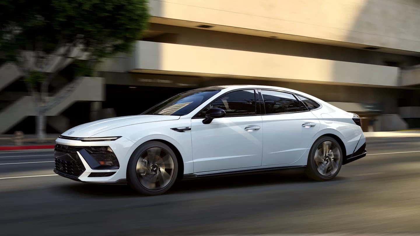 A white 2026 Hyundai Sonata driving through the city, showcasing its sleek modern design and aerodynamic profile.