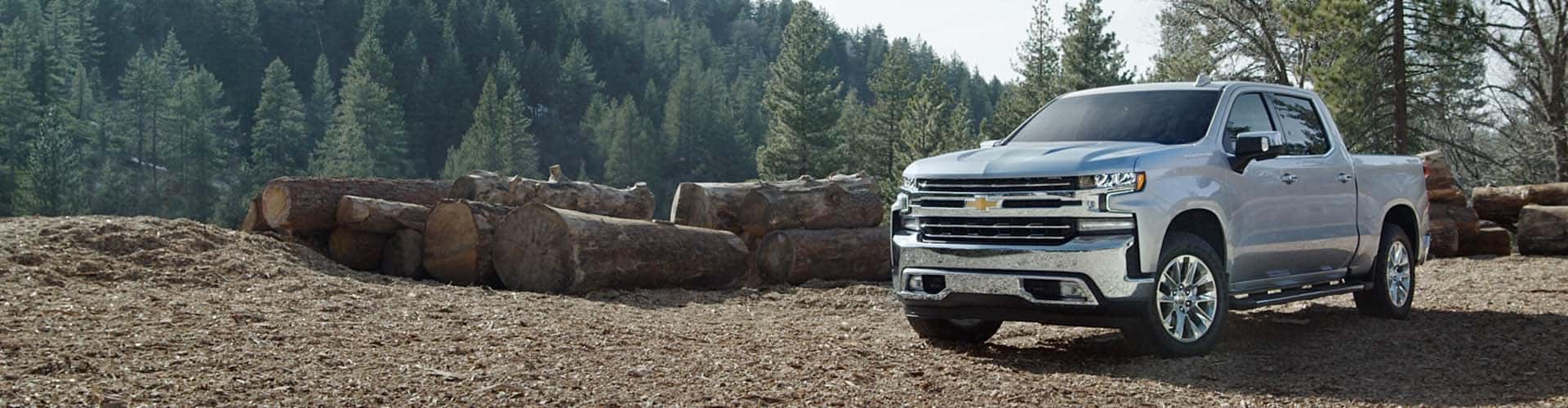 Performance Chevrolet is a Car Dealership near Poplar Branch, NC | 2021 Silver Chevy Silverado 1500 Parked In Front of a Logging Farm in the Mountains