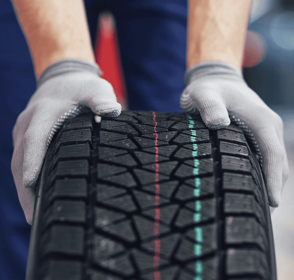 What is a Tire Rotation? at Performance Chevrolet | Person with grey gloves and blue pants is pushing a new tire on the ground