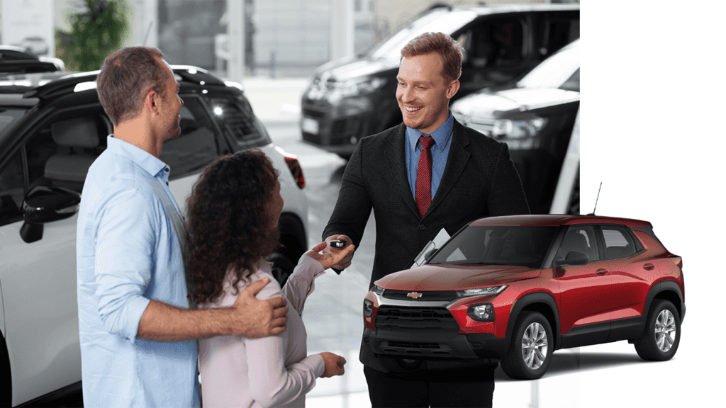 Best Time To Buy At Performance Chevrolet in Elizabeth City, NC | Red 2022 Chevrolet TrailBlazer with a background photo of a sales person handing car keys over to a couple for a test drive