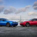 Dodge Charger parked near a waterfront with two red and blue performance sedans.