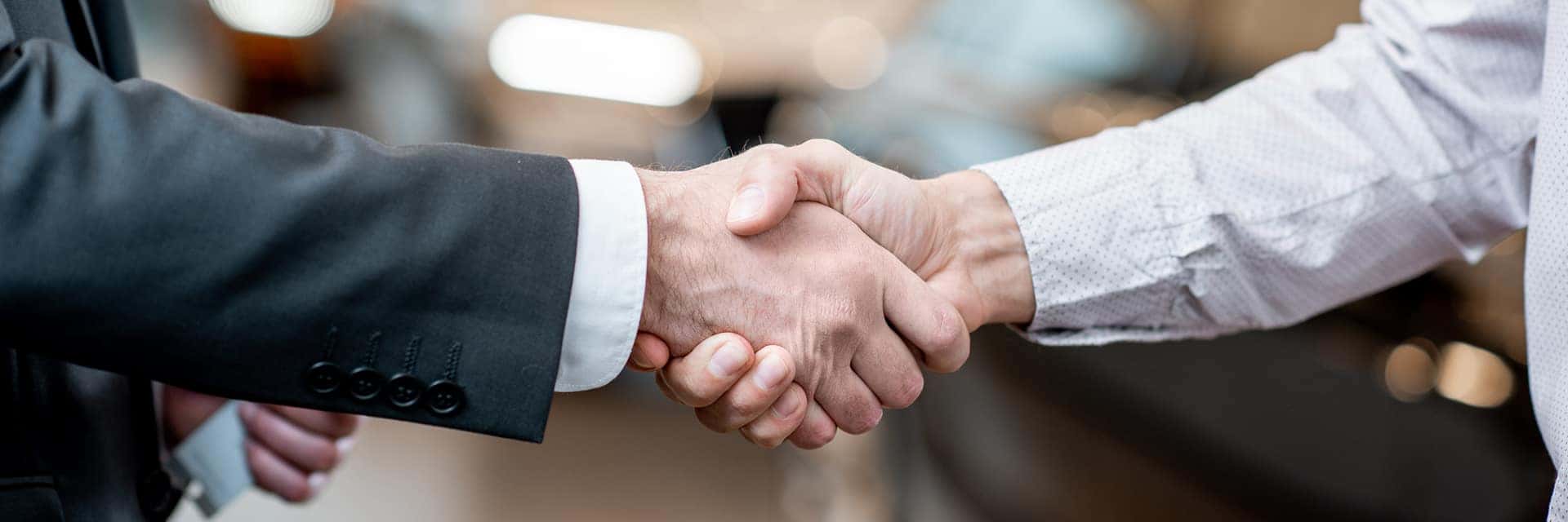 two people shaking hands in front of vehicles